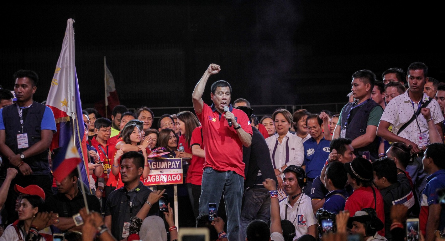Duterte stands with his fist raised and a crowd of people stand behind him