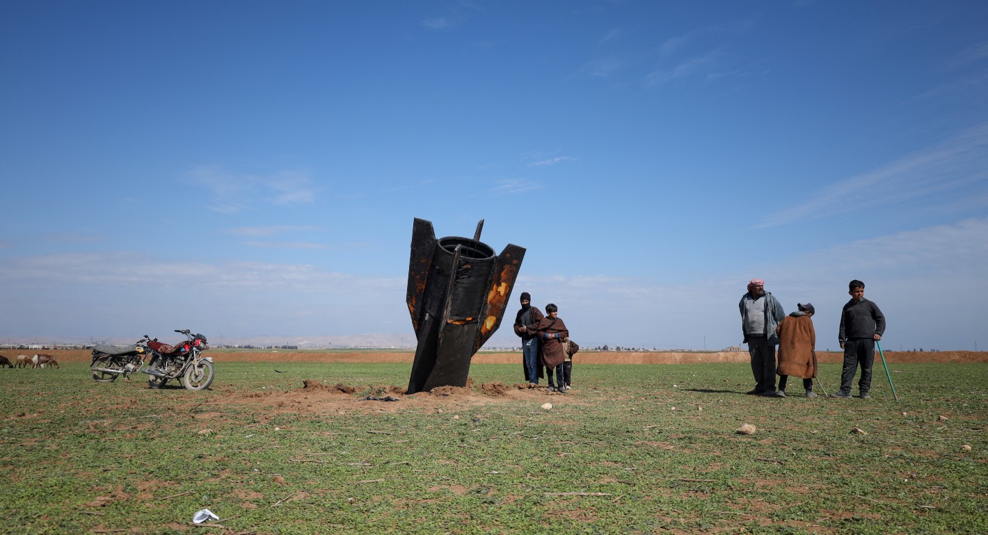 A missile tail embedded in the ground in an open field with green ground cover and a blue sky.