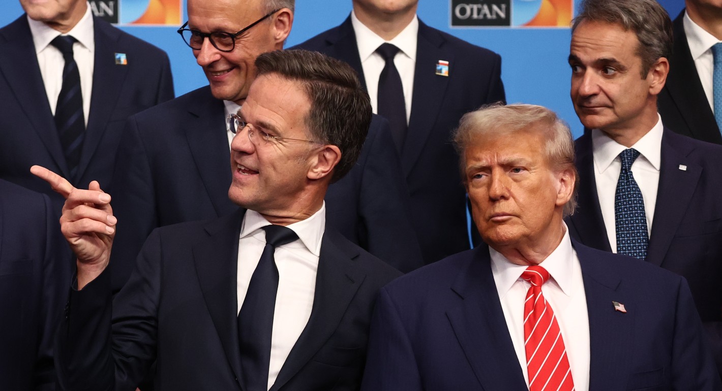 Rutte and Trump are two white men in suits. They look off to the left of the camera and stand in front of a row of other men in suits.