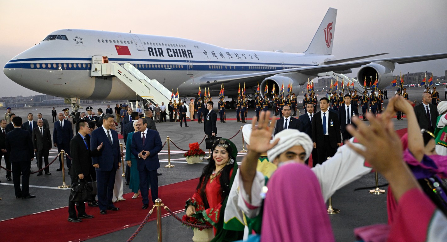 People dancing in the foreground, with a group of people in suites watching and an Air China plane in the background