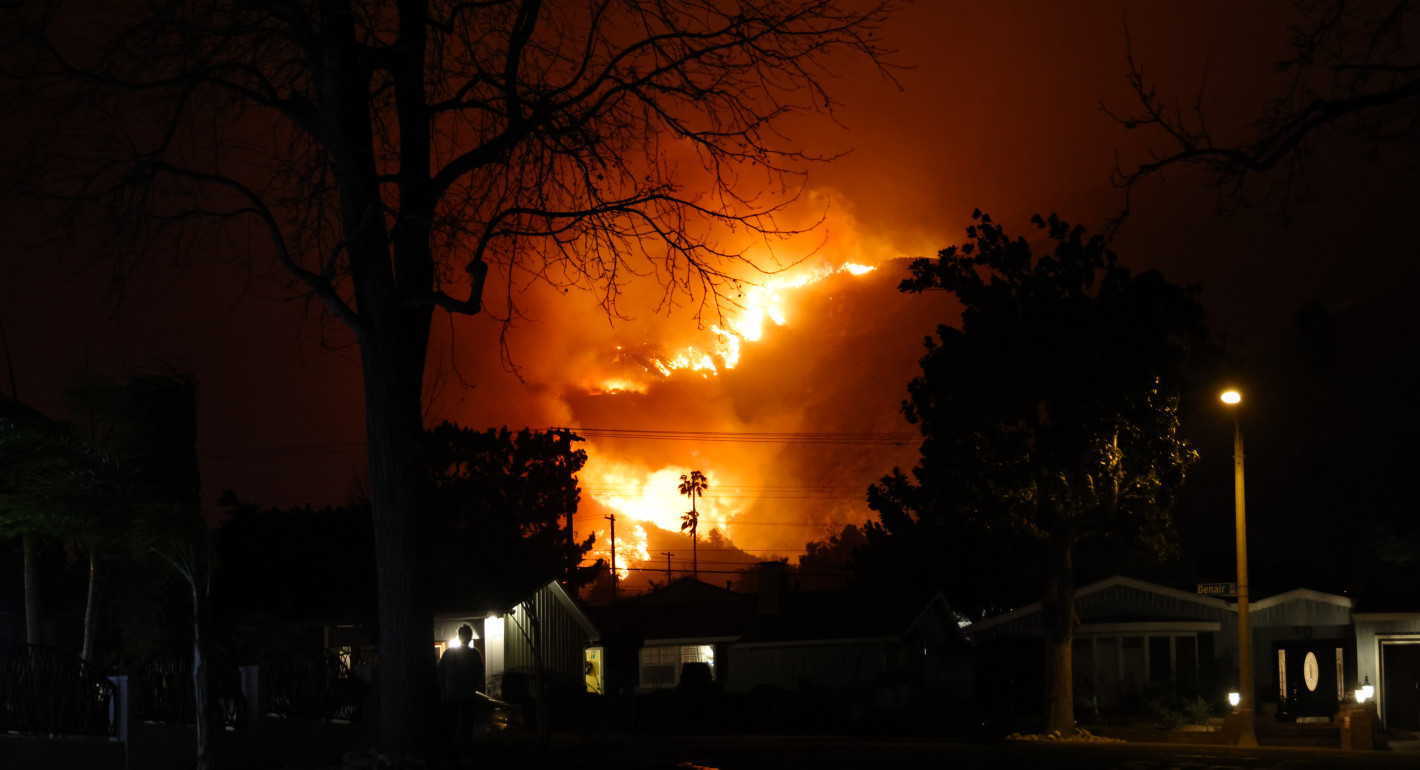 Photo of flames behind palm trees in a residential neighborhood in Altadena, California.