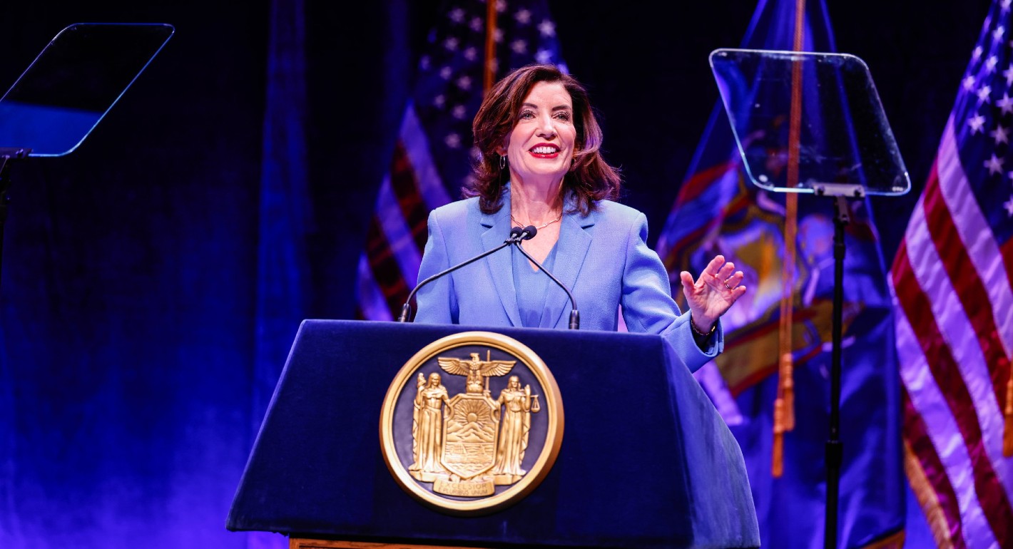 Hochel stading behind a dais, with a hand raised