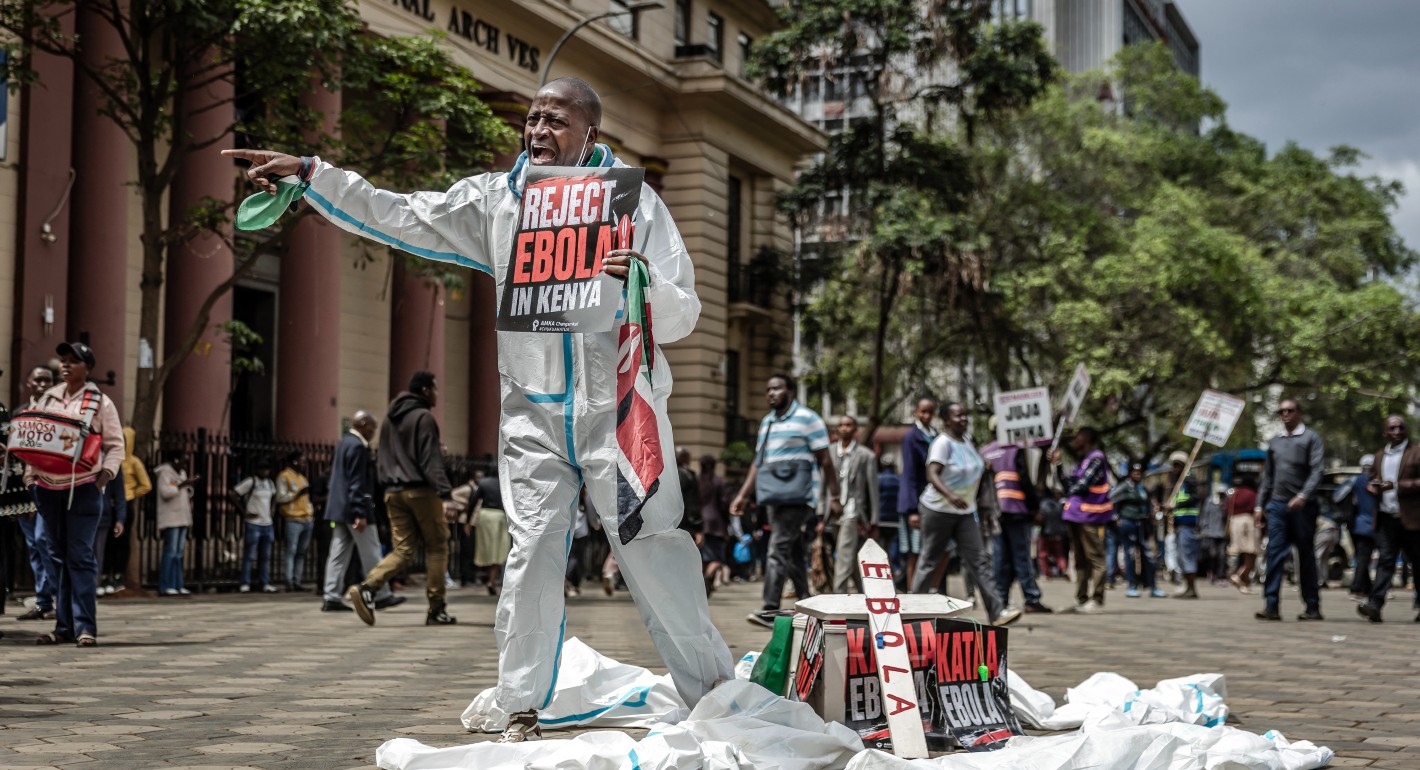 Person pointing and shouting while holding a protest sign against the Ebola facility