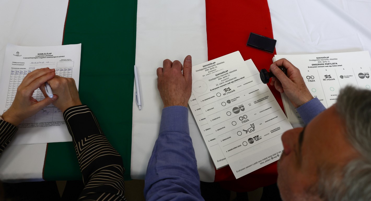 Photo of a person's hands holding a Hungarian voting card with a Hungarian flag tablecloth in the background.