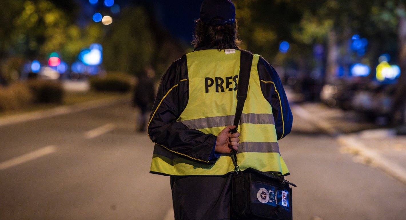 A person faces away from the camera wearing a yellow jacket with "PRESS" printed across the back