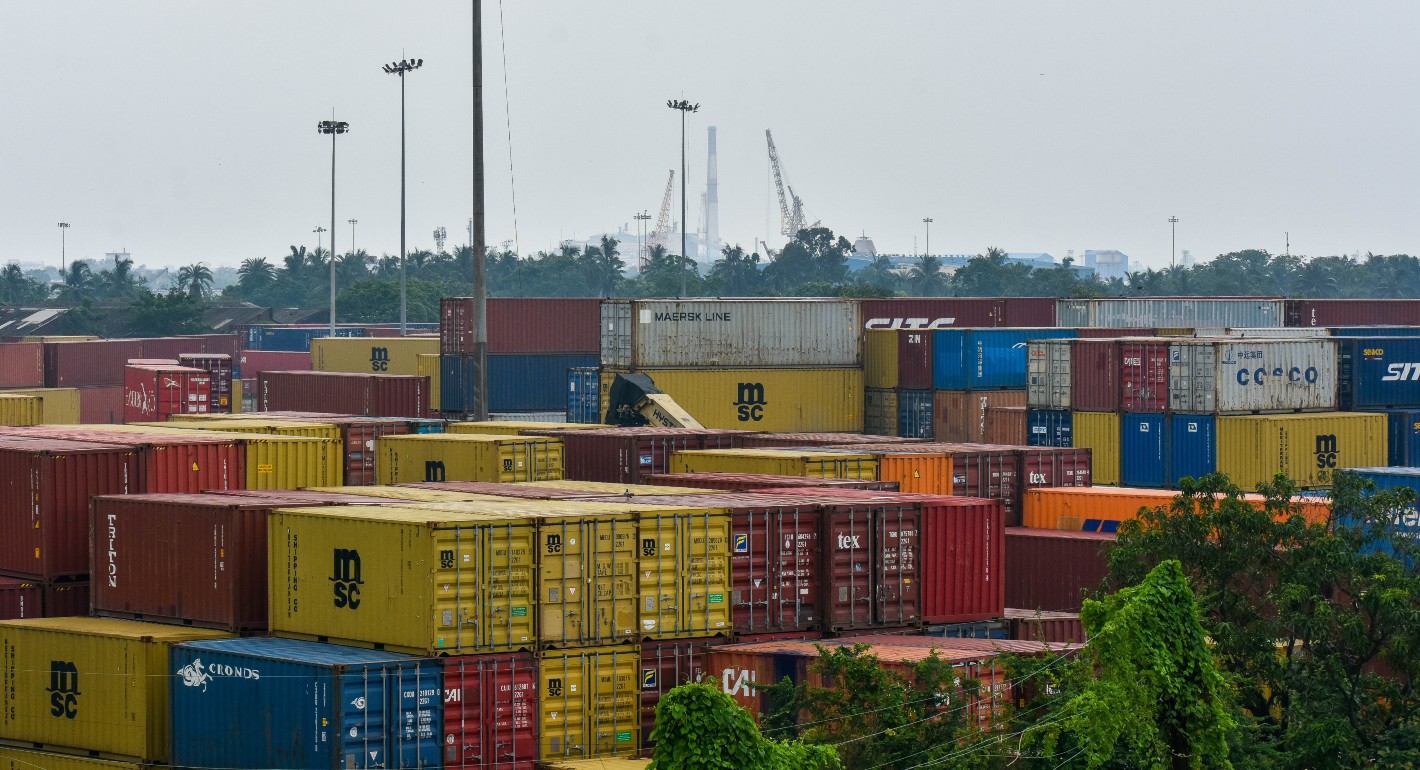 Photo of shipping containers stacked against a cloudy sky.