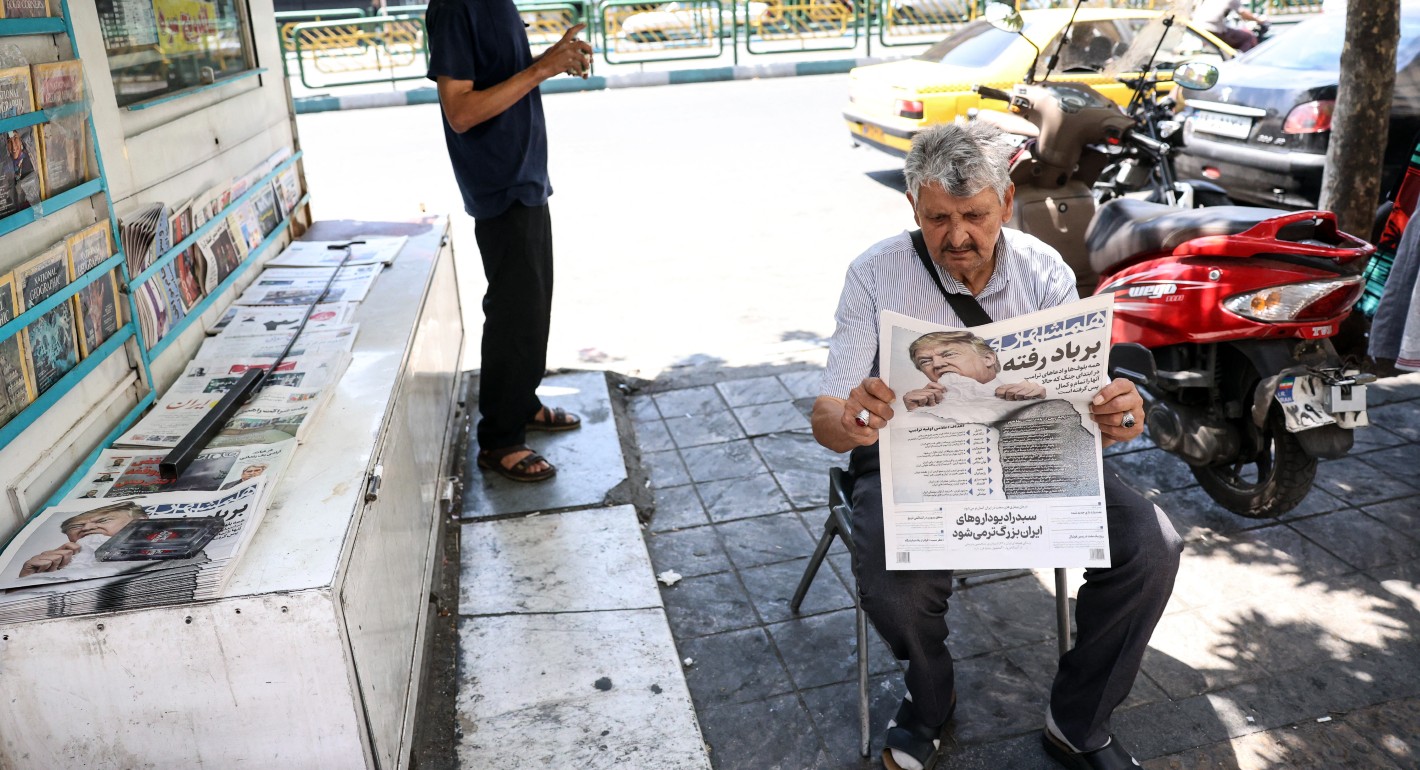 Man sitting in a chair reading a newspaper with Trump's face above the fold