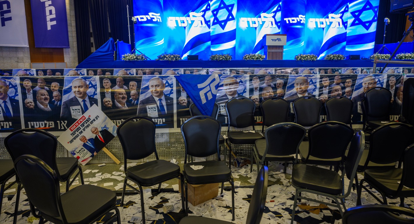 empty chairs and posters in front of a stage, with a big screen showing the Israeli flag