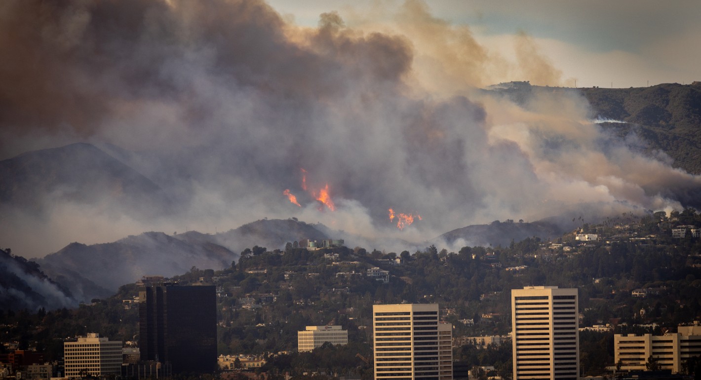 Wide shot of a wildfire burning a hillside near buildings