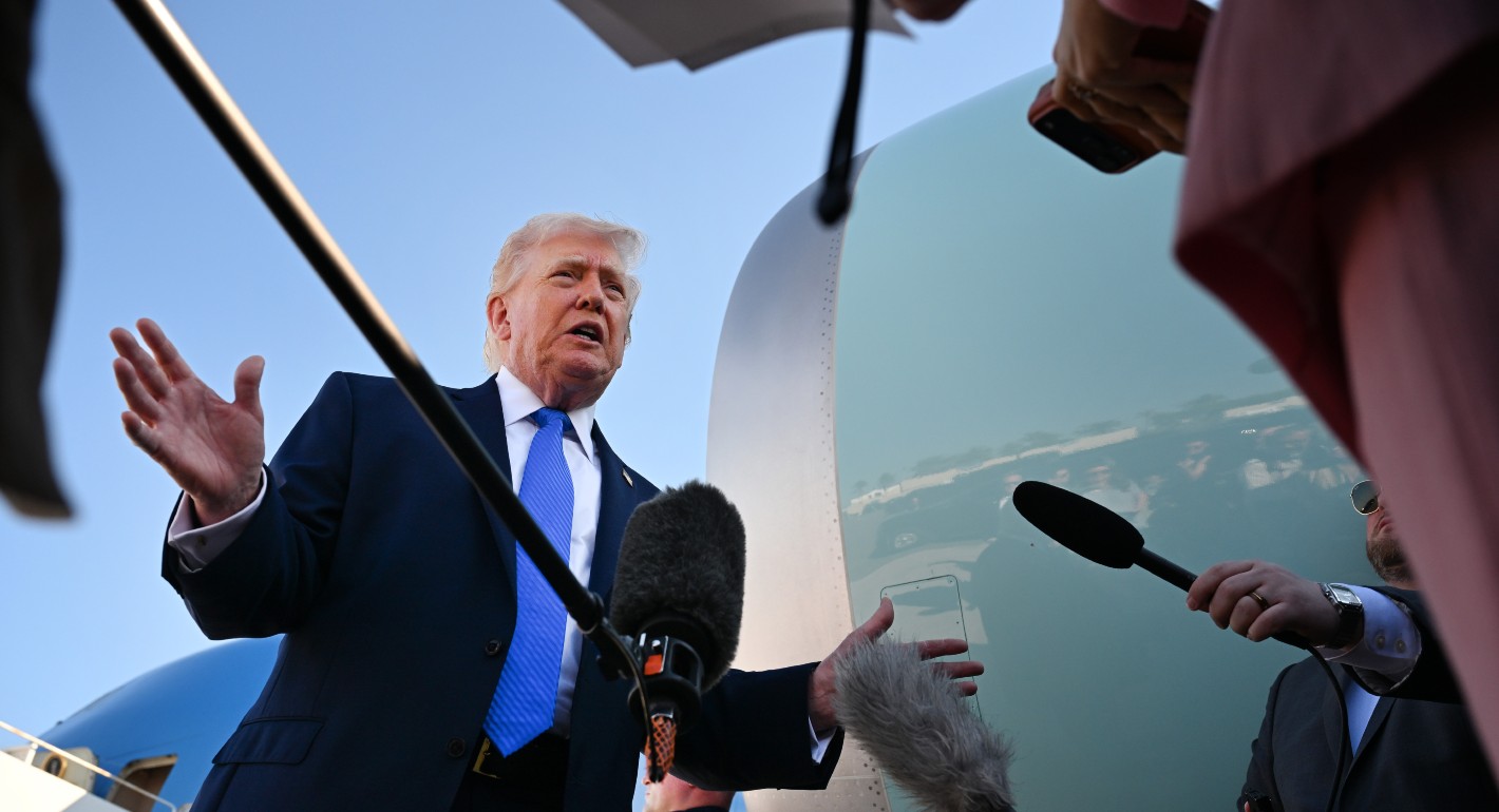 Trump with arms out, surrounded by mics