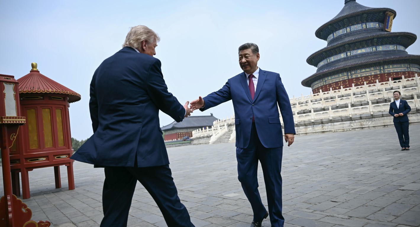 Trump walking toward Xi, both with arms extended to shake hands