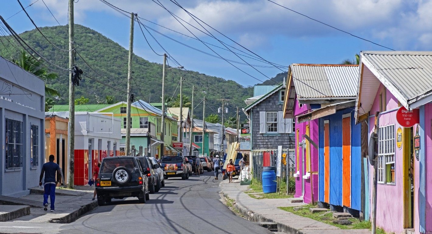 Colorful houses (pink, cobalt blue, bright orange, mint green) line a road curving to the right. Cars and electricity poles run on the side of the street