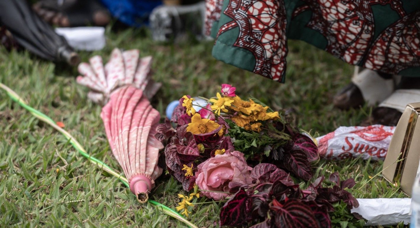 Yellow and pink flowers and a pink umbrella lay on green grass in the center of the image