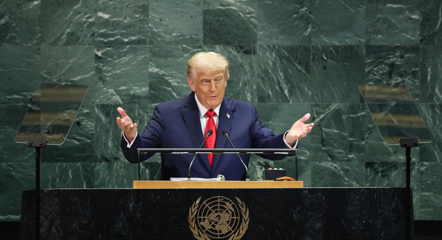 Trump stands in front of a podium with the UN logo. the background is a green marble stone wall