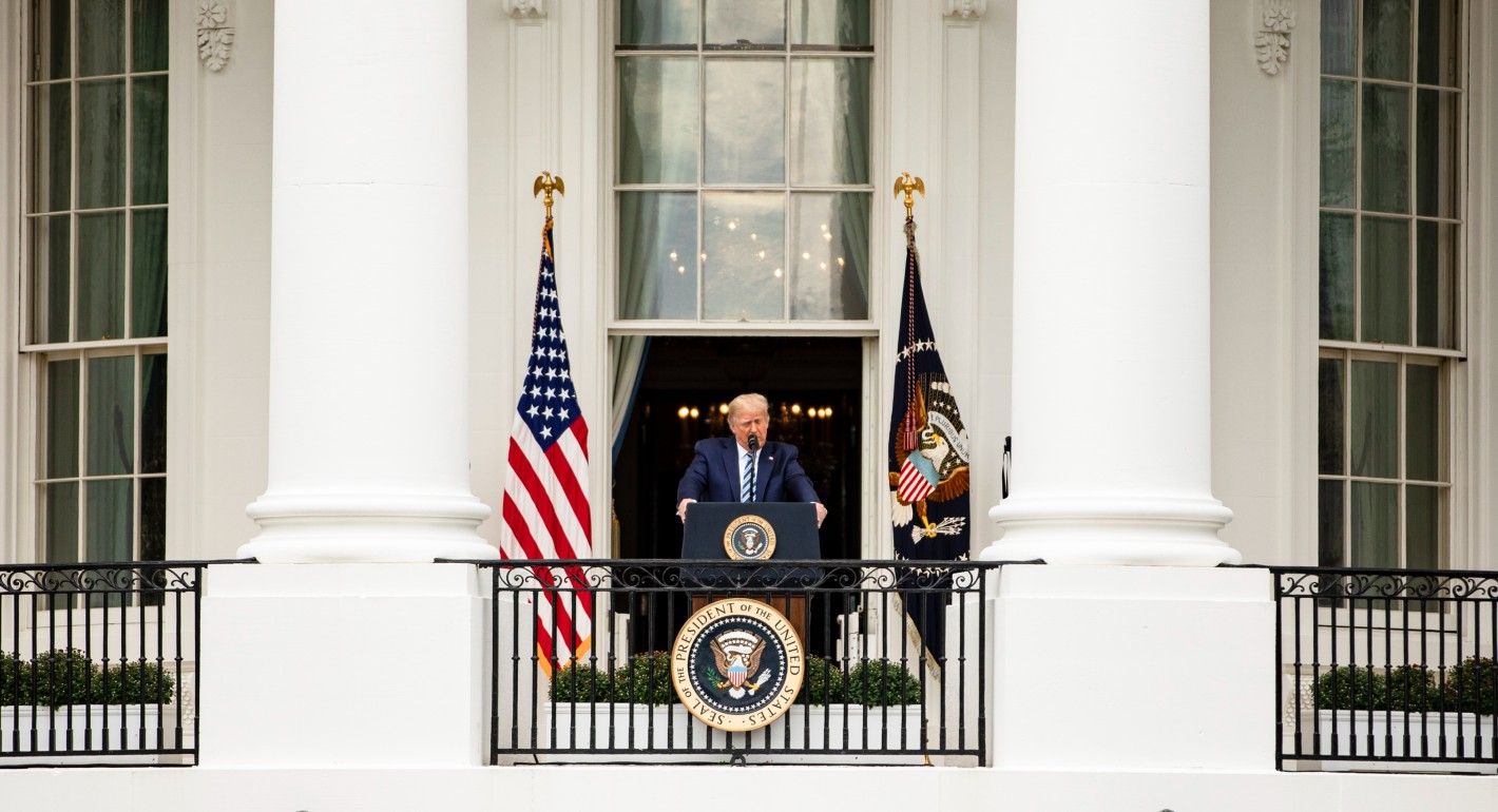 Trump stands on White House balcony behind presidential seal and between U.S. and presidential flag