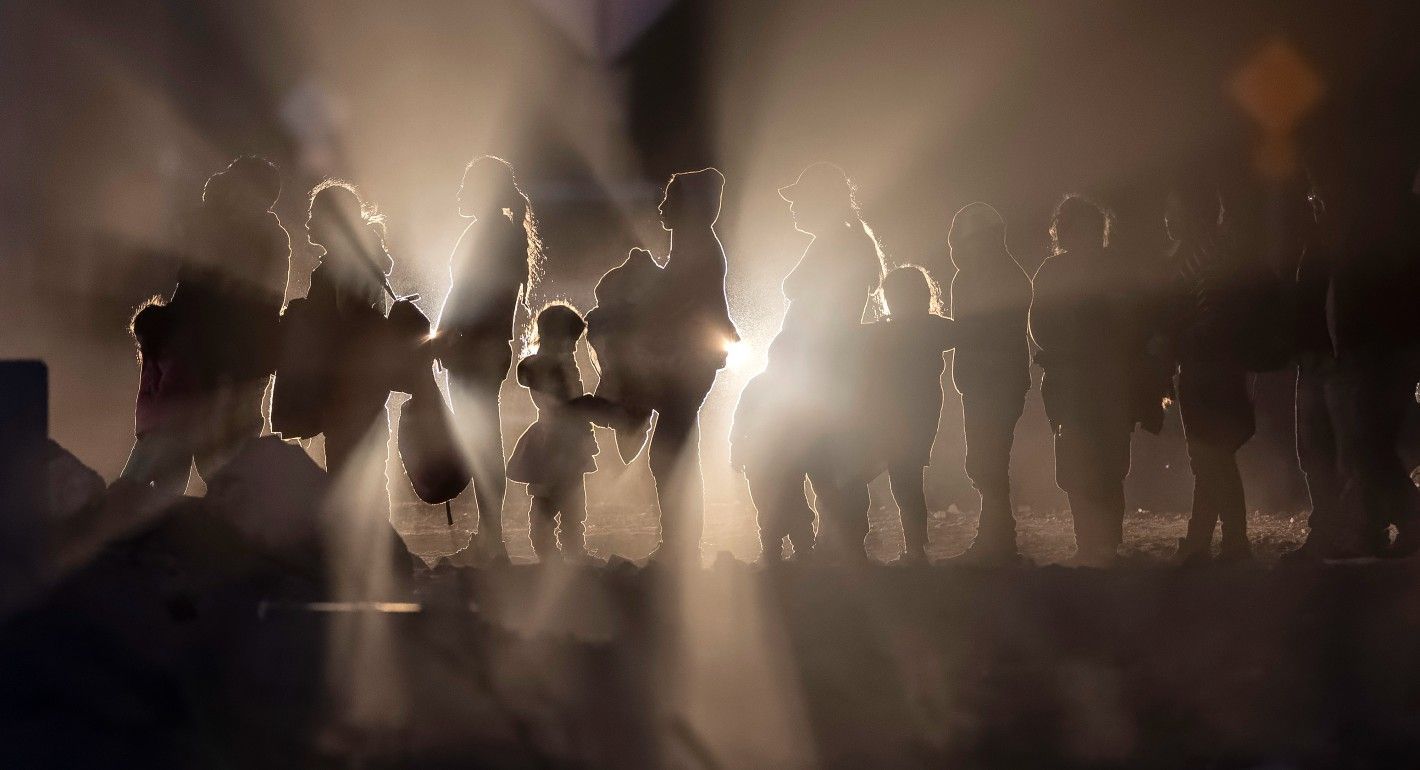 people waiting in a line, lit only by car headlights