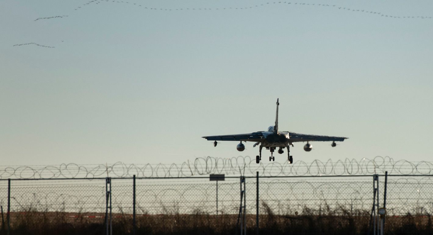 Photo of an airplane landing above a barbed wire fence.