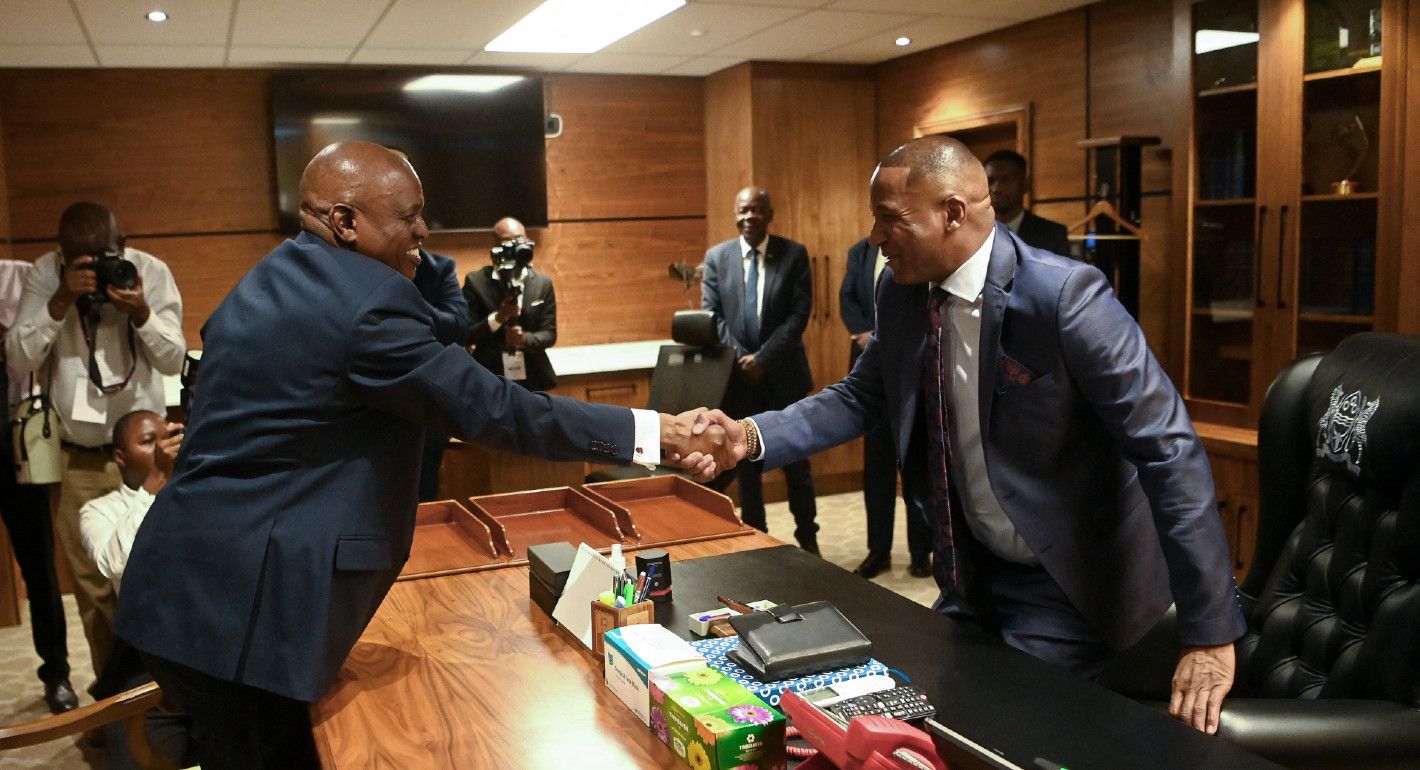 Photo of Duma Boko and Mokgweetsi Masisi shaking hands across a wooden desk.