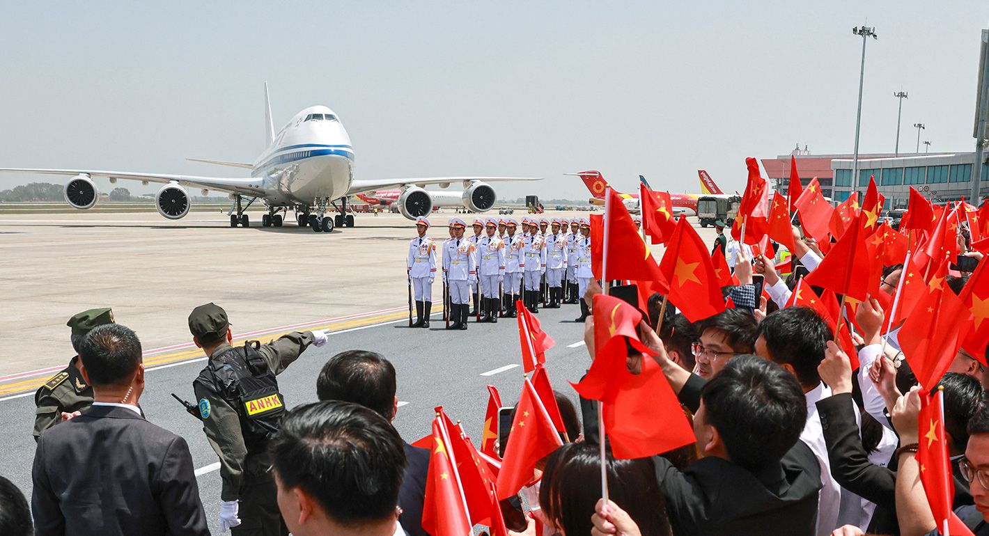 People wave Chinese flags as the plane carrying Chinese President Xi Jinping arrives for a two-day state visit at Hanoi's Noi Bai International Airport in Hanoi on April 14, 2025