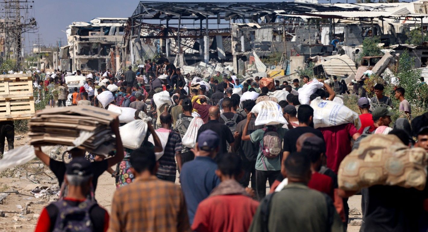 crowds of people carrying large bags amid bombed-out buildings
