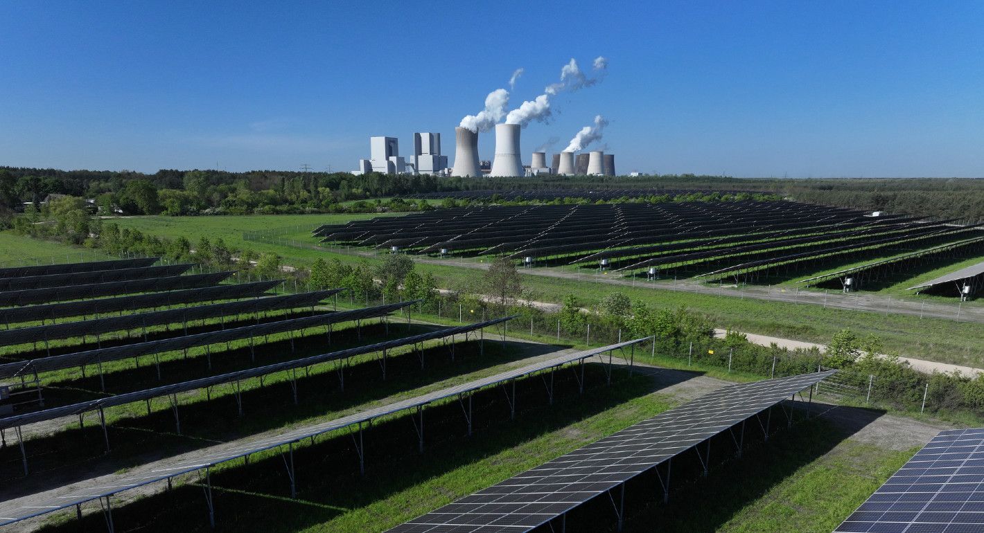 Fields of solar panels in the foreground, with a coal plant in the background
