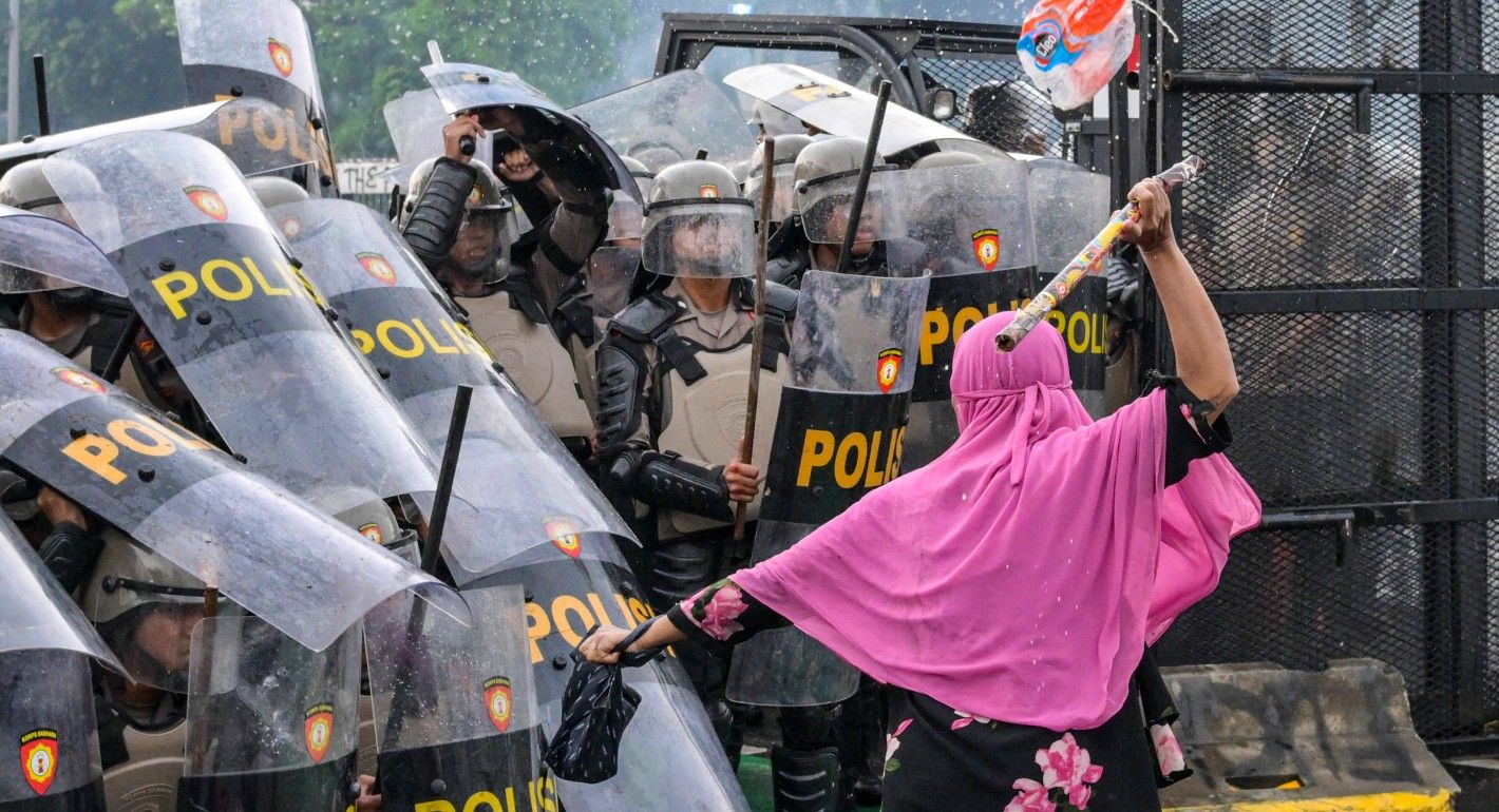 Woman swinging a baton at police officers with riot shields