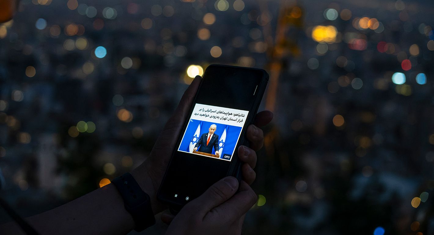 ranian girl reads news on her smartphone as people gather in the heights of north of Tehran, Iran, to watch a view of the exchanges of strikes between Israel and Iran on June 14, 2025. The news is a piece of comment by Israeli PM Netanyahu saying that "you will soon see Israeli jets in Tehran's sky". 