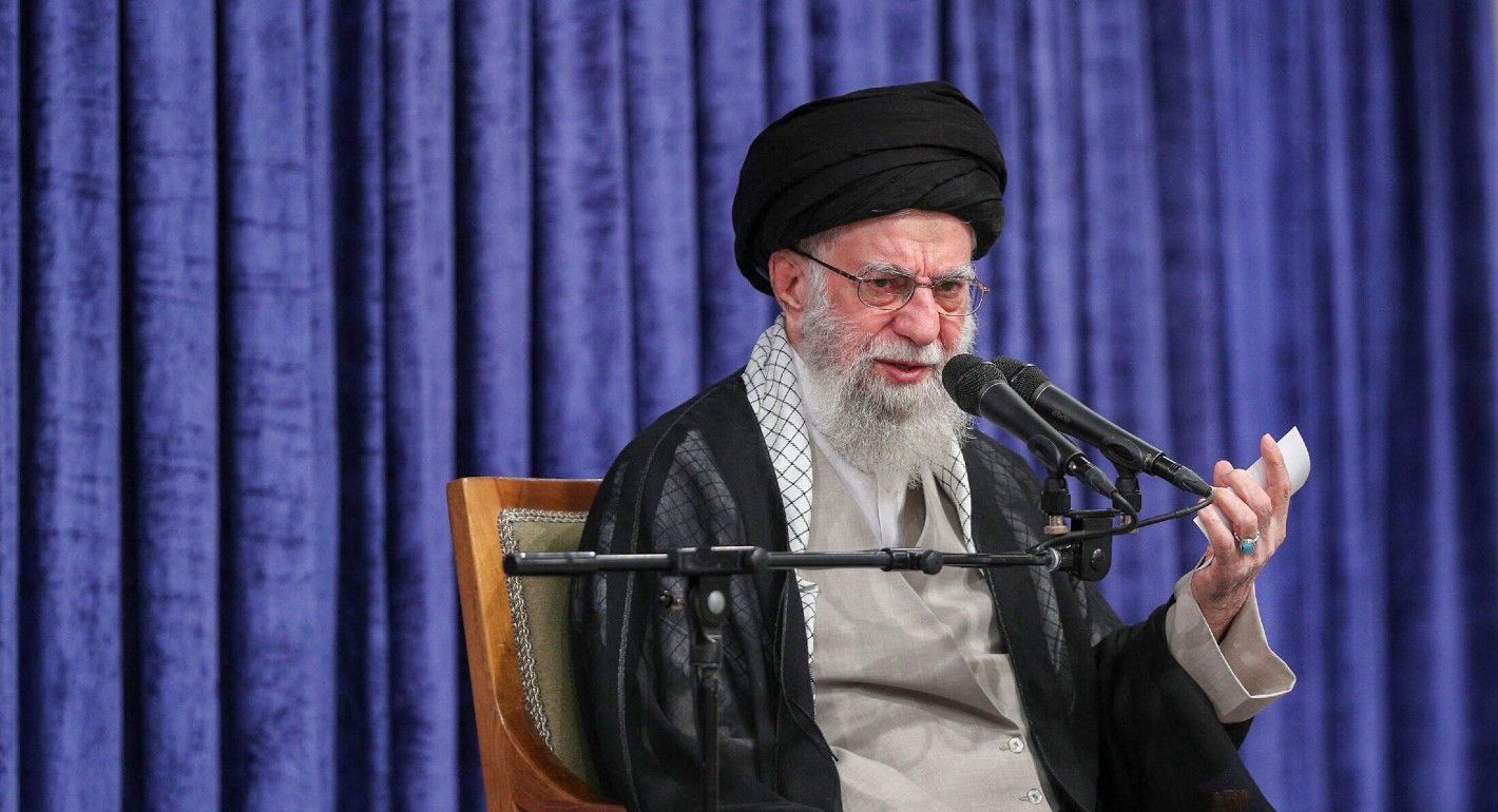Khamenei sitting in front of a purple curtain speaking into a mic