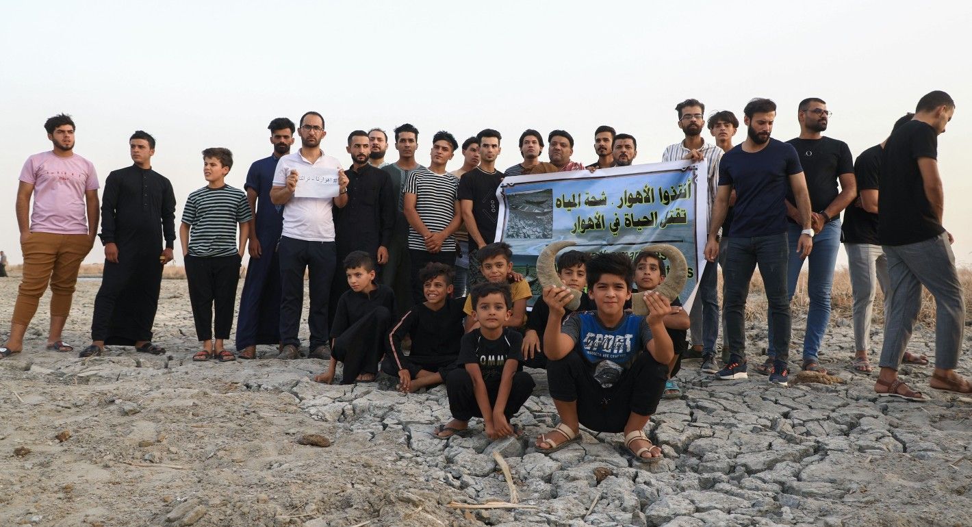 Photo of a group of Iraqi protesters holding a banner over dry, cracked ground.