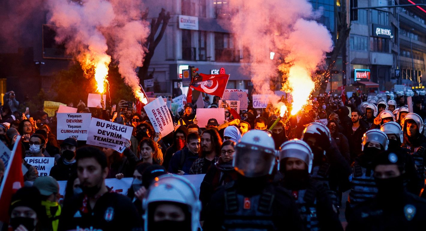 People holding signs and burning flares while surrounded by riot police