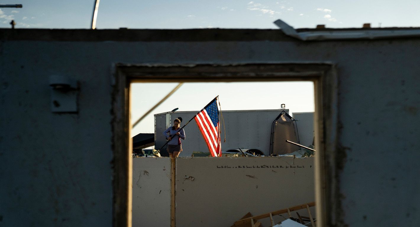 Woman standing in the remains of a home holding an American flag