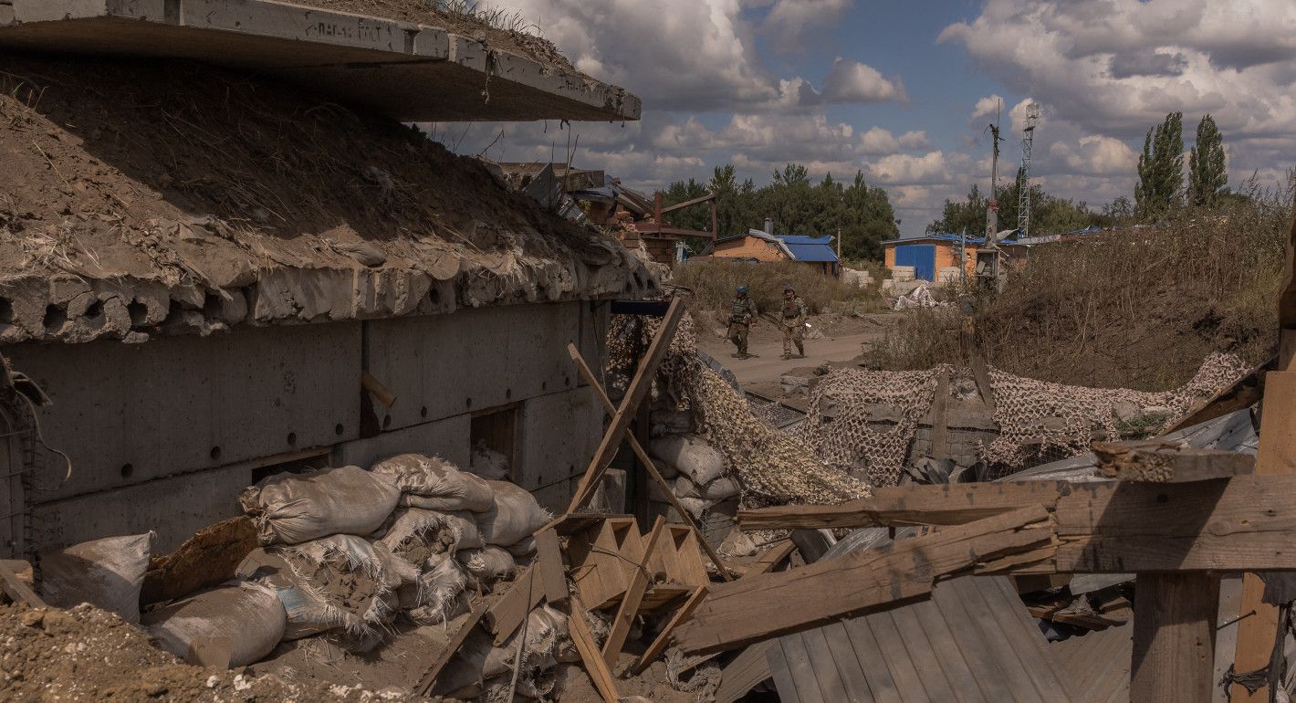 Destroyed buildings in the foreground, with soldiers walking in the background