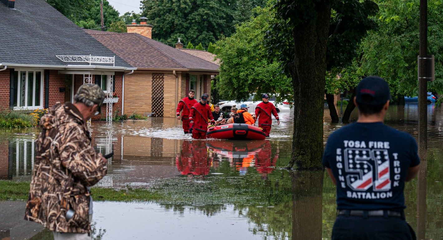 First responders walking people in a boat past flooded houses